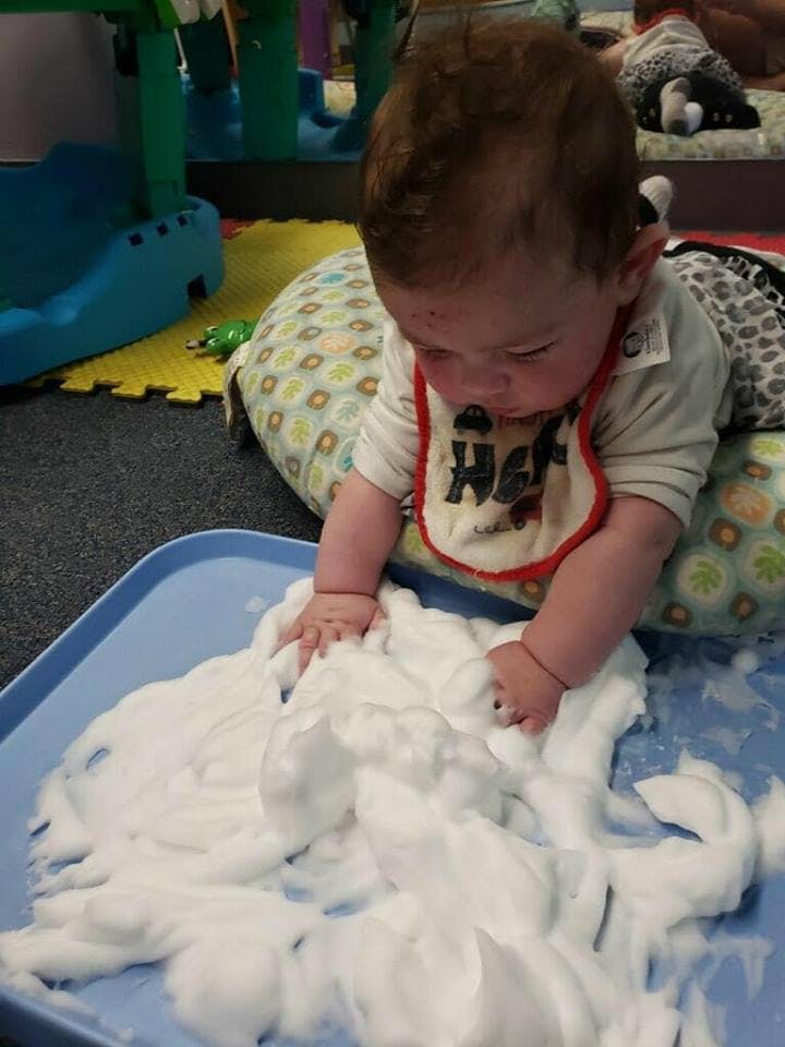 Child playing with white foam on a blue tray