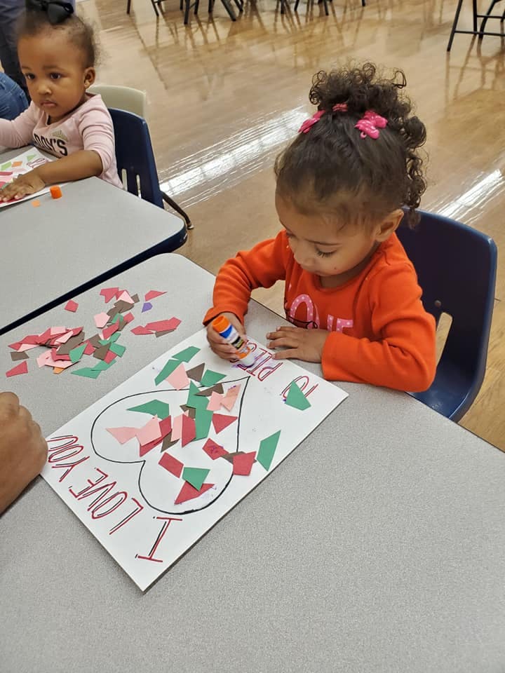 Child gluing paper pieces onto a heart-shaped drawing