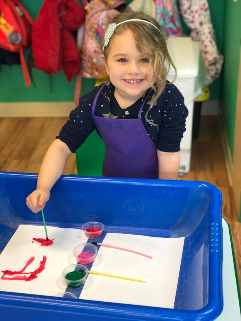 Child in an apron painting with a brush in a blue tray