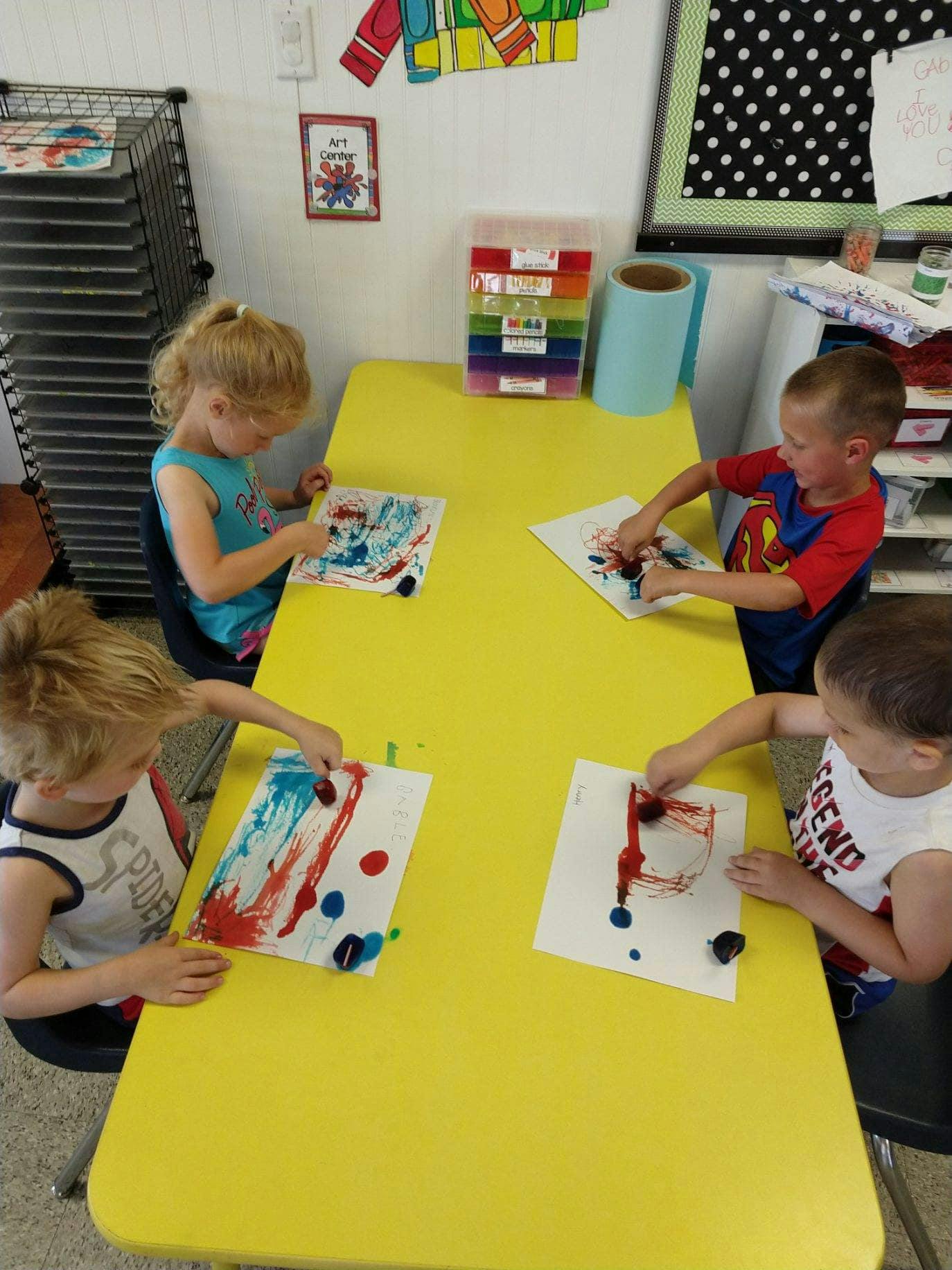 Four children finger painting at a yellow table