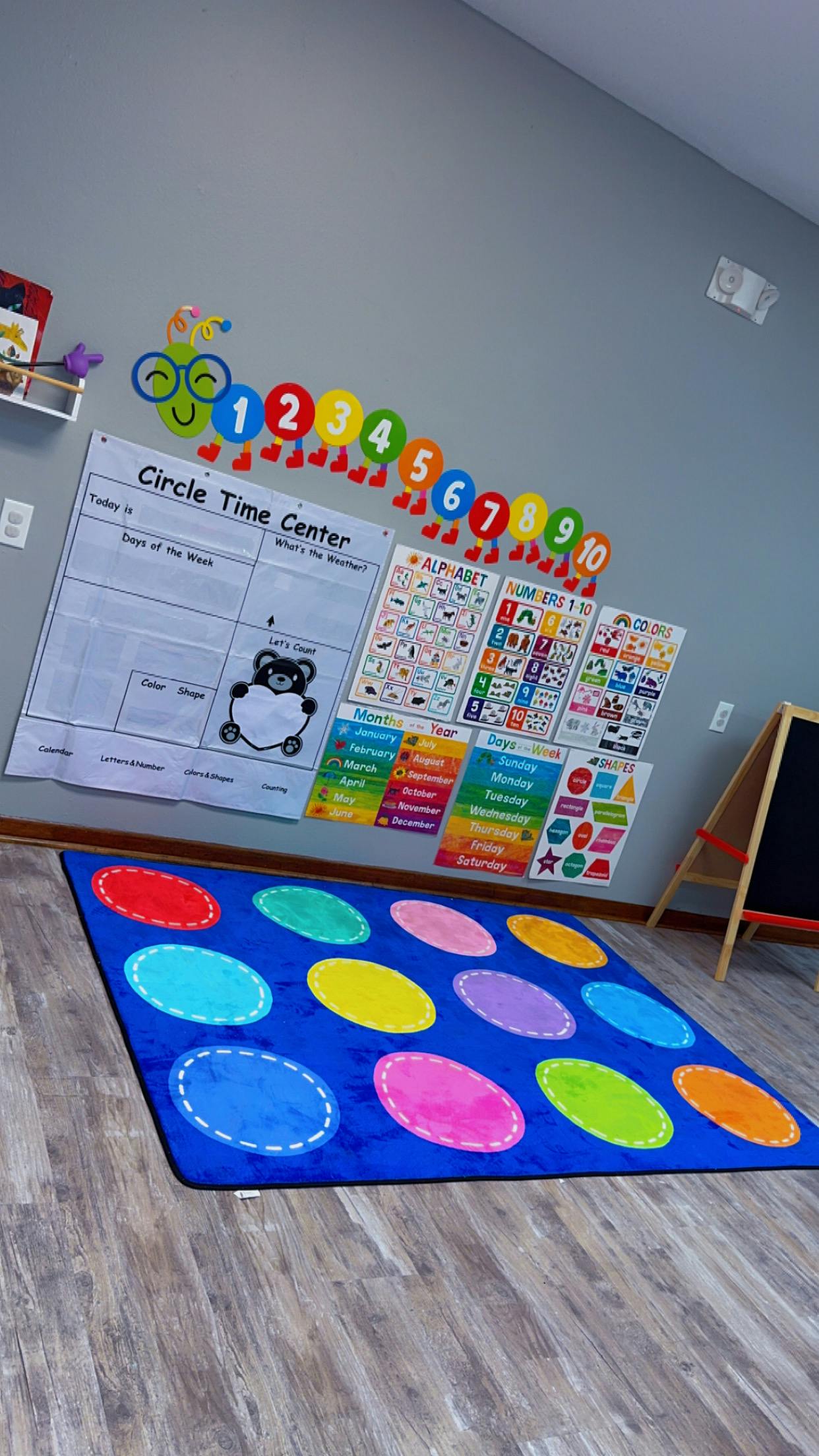Classroom wall with educational posters and a blue rug with colorful circles