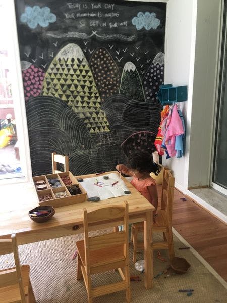 Child drawing at a small wooden table in front of a chalkboard wall
