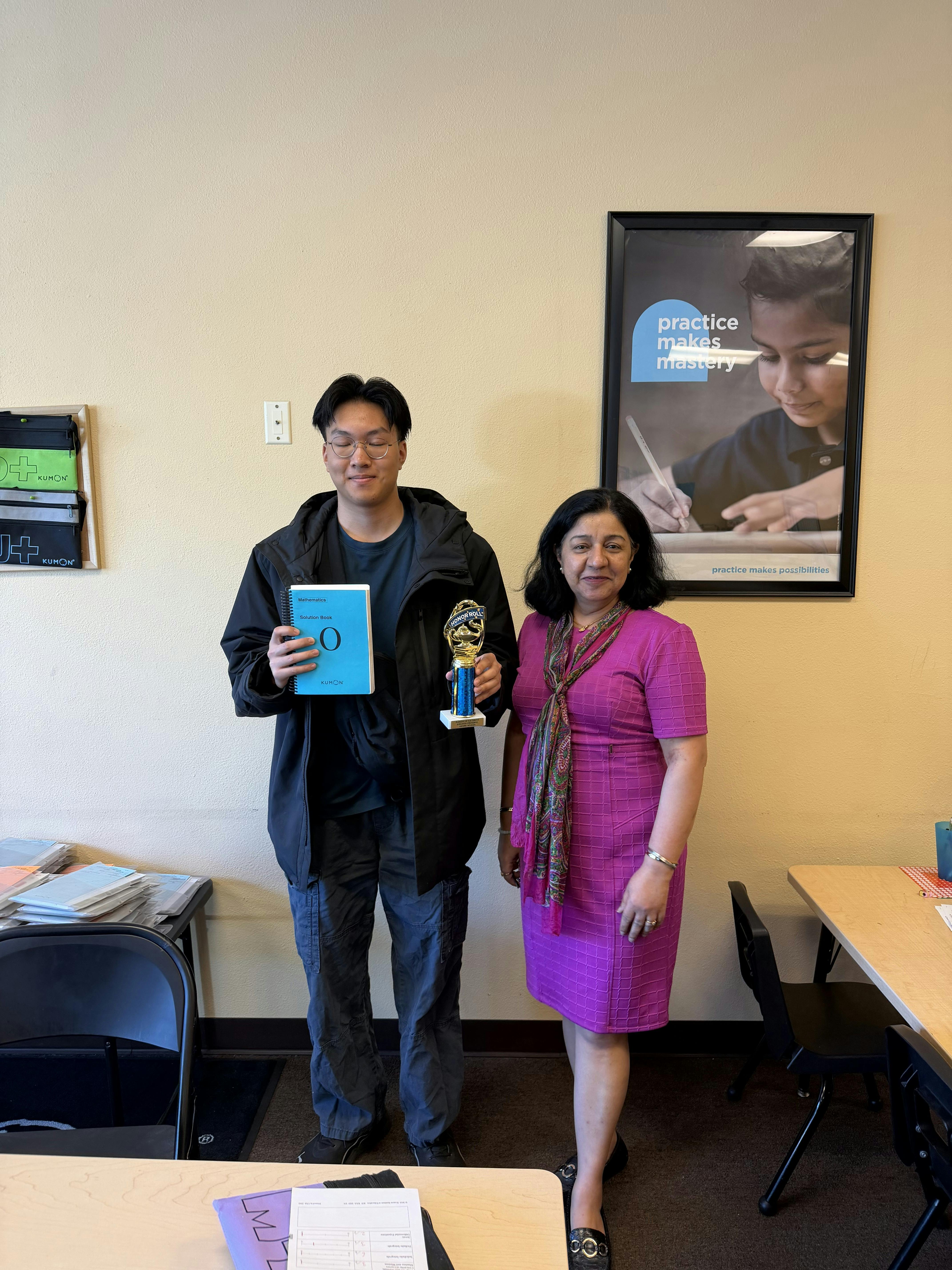 Person holding a trophy and book standing with a person in a pink dress