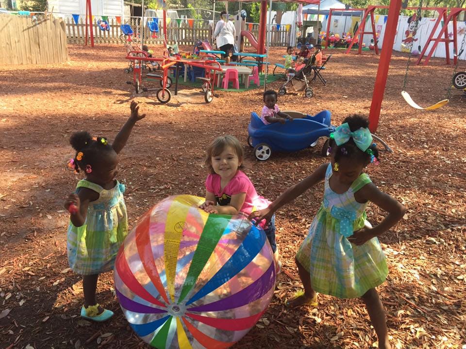 Three children playing with a large colorful ball on a playground