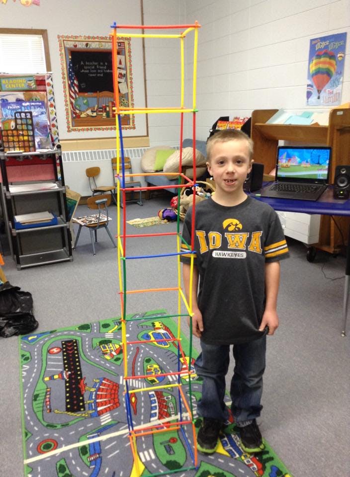 Child standing next to a tall structure made of colorful plastic tubes