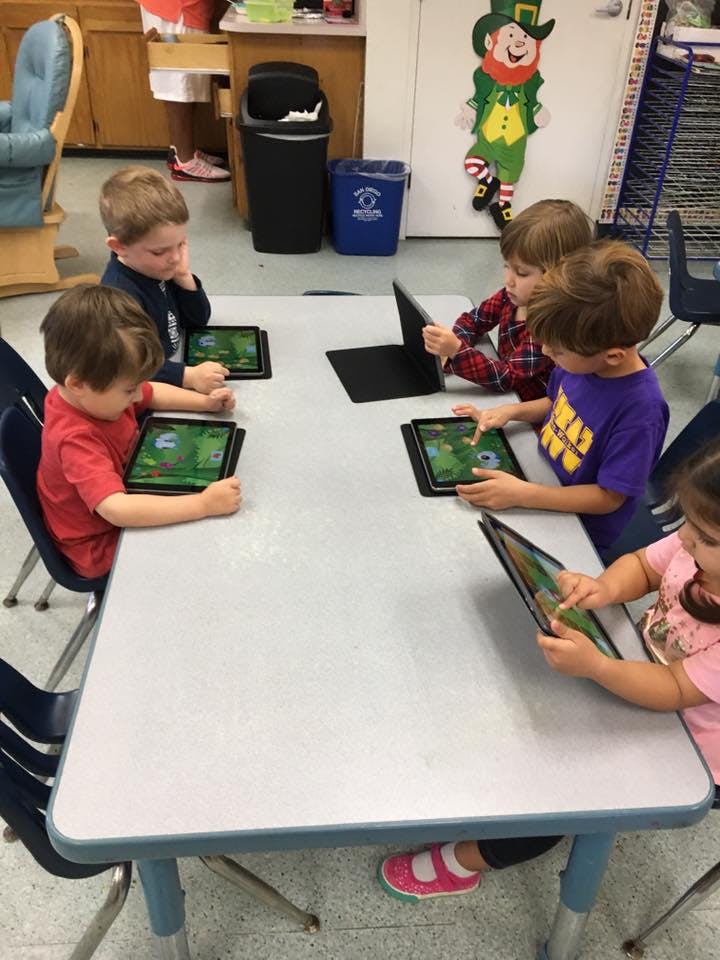 Children sitting at a table using tablets