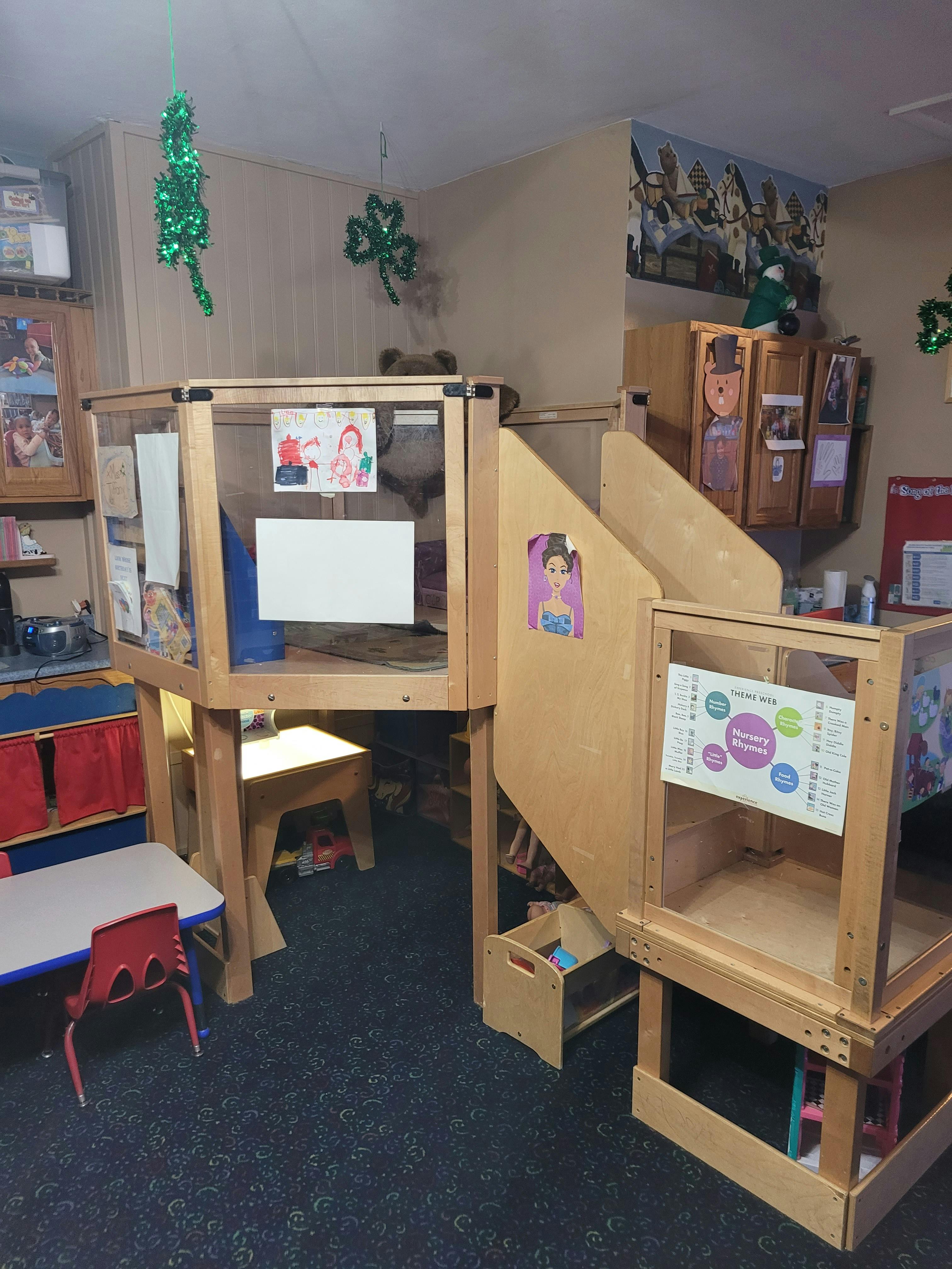 Classroom corner with wooden shelves, table, chair, and a 'Nursery Rhymes' chart