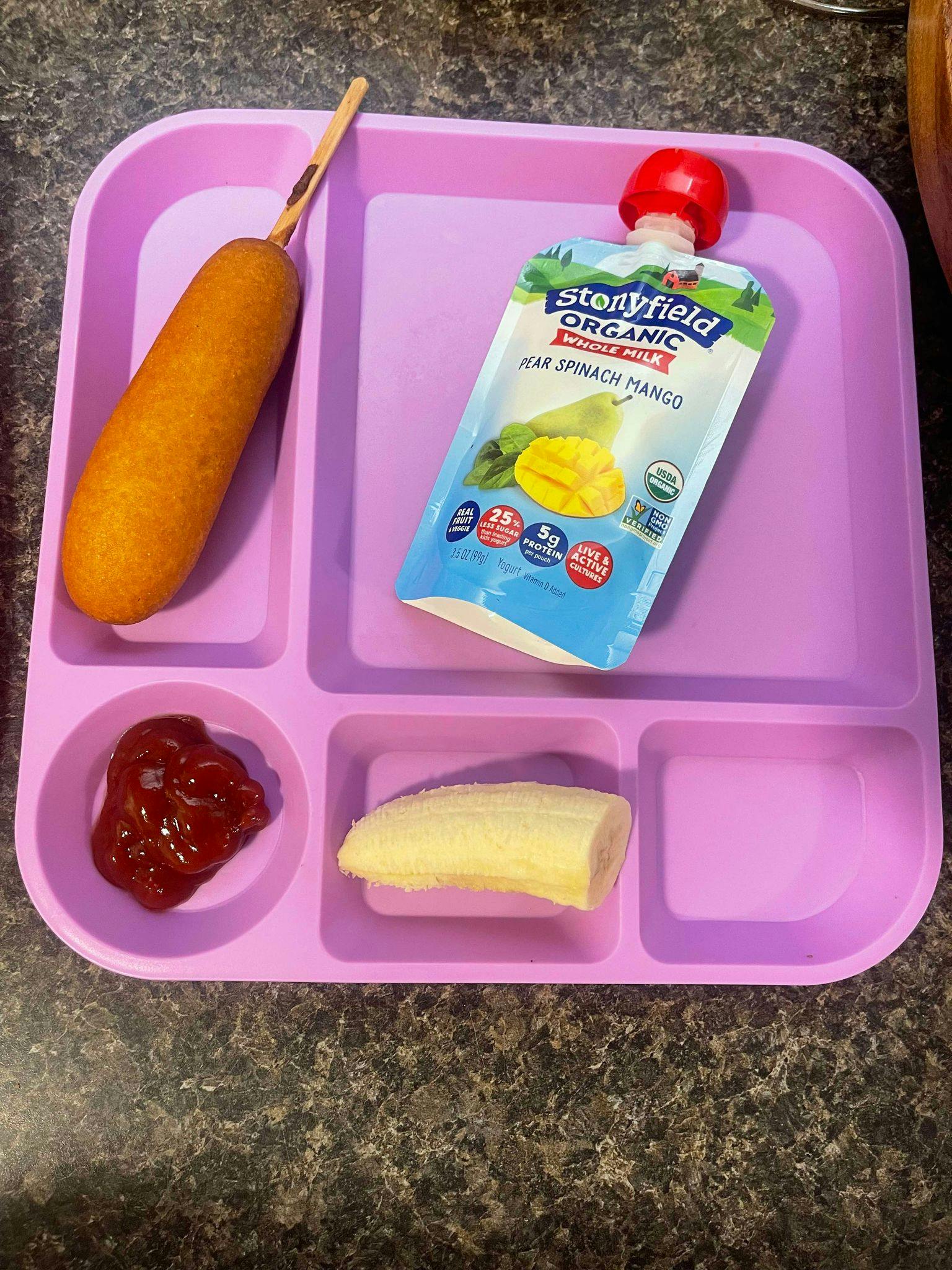 Corn dog, fruit pouch, ketchup, and banana on a divided tray