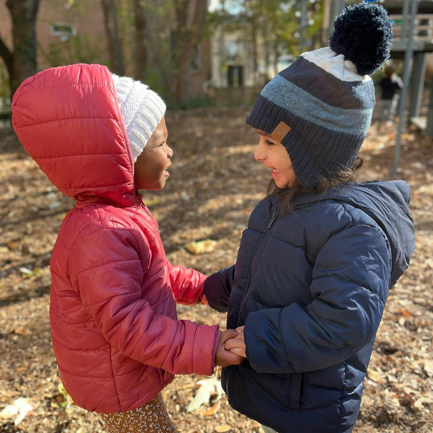 Two children in winter coats and hats holding hands outdoors