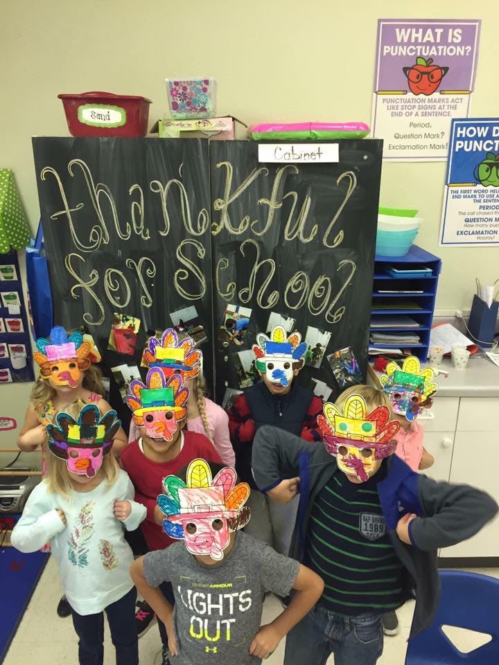 Children wearing colorful masks in front of a chalkboard that says "Thankful for School"