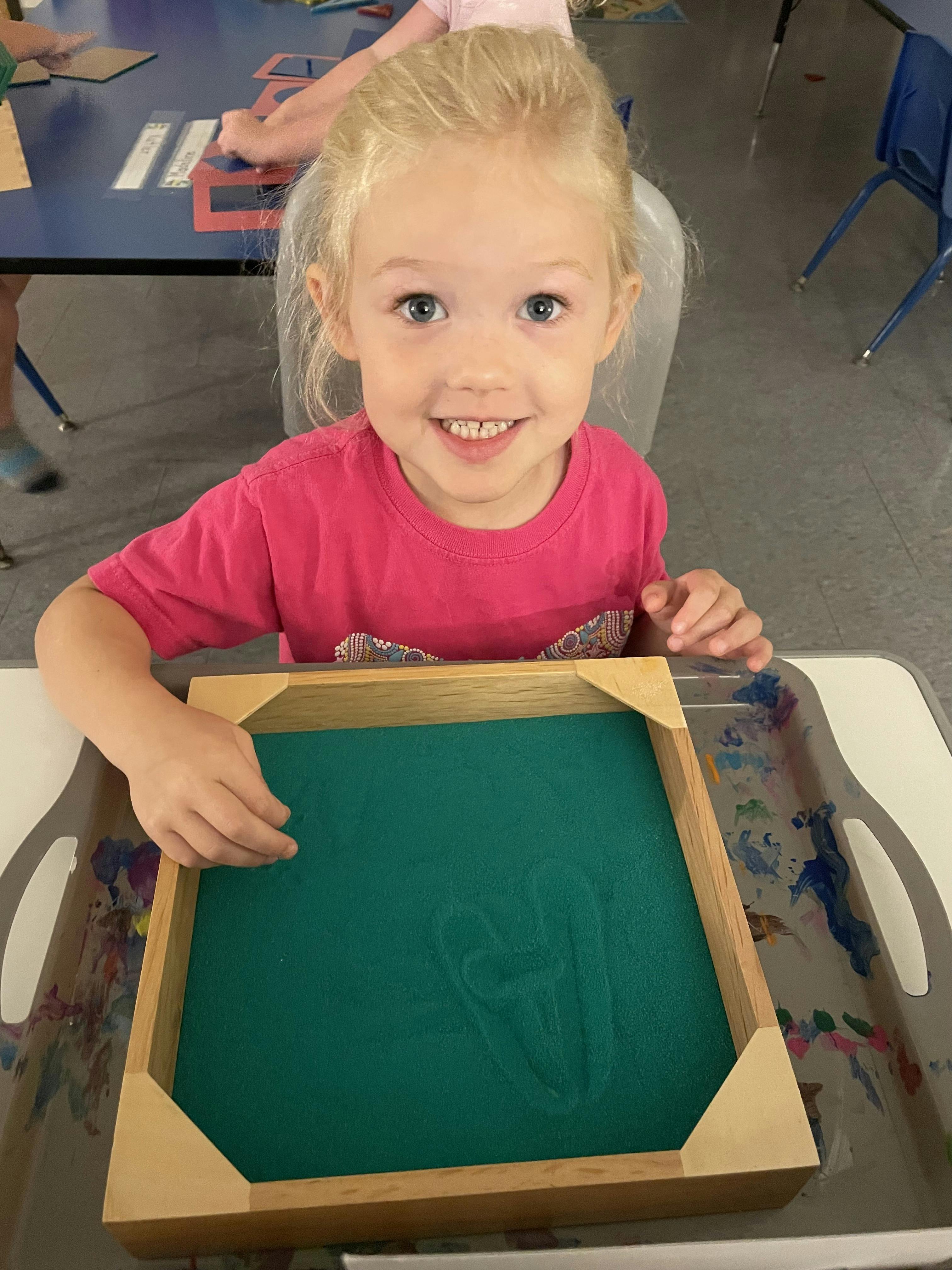 Child smiling while sitting at a table with a sand tray