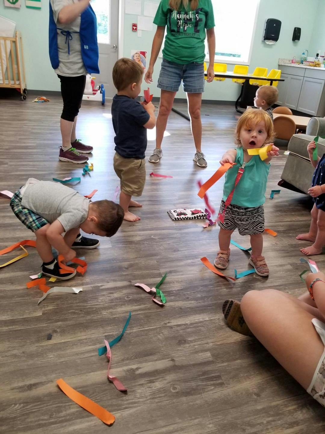 Children playing with colorful paper streamers on a wooden floor