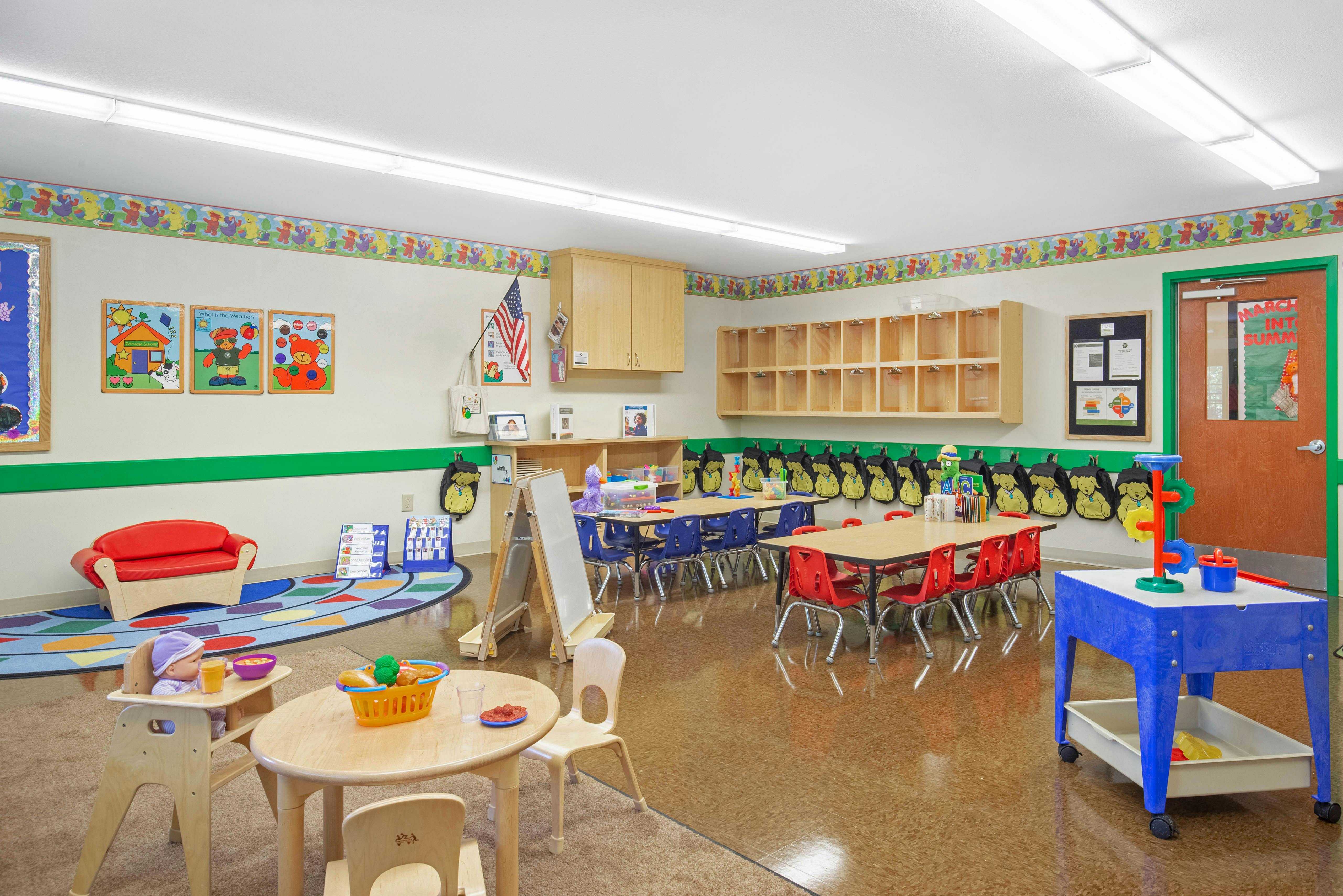 Doll sitting in a high chair with a bowl and glass on a small table in a classroom