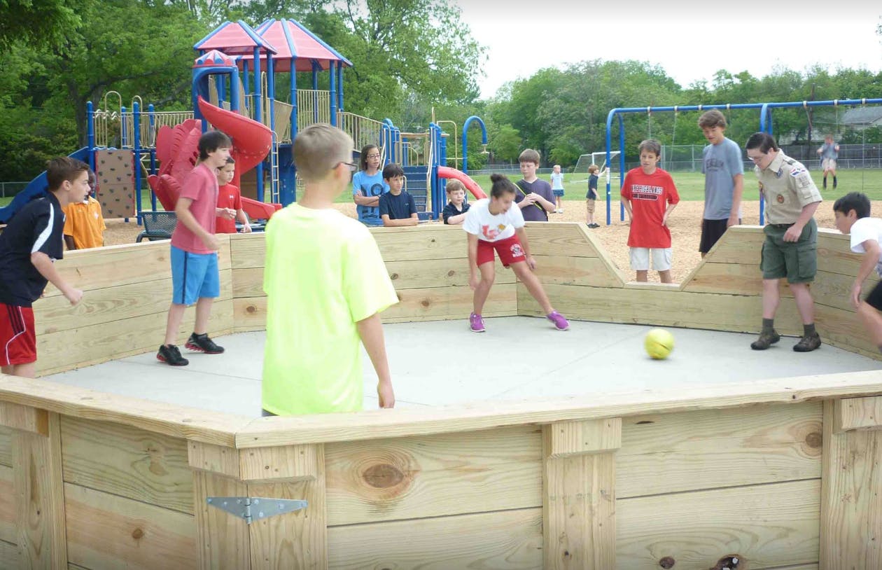 Children playing gaga ball in a wooden pit on a playground