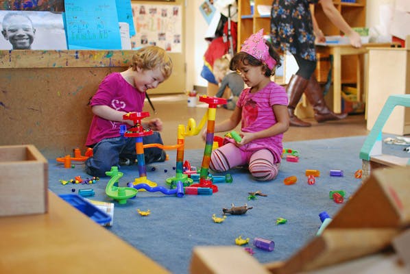 Two children playing with a colorful marble run on a blue carpet in a classroom