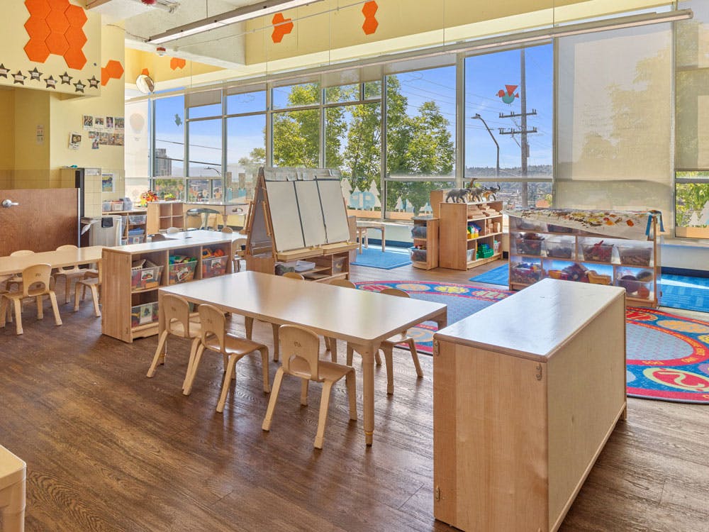 Children's classroom with small tables and chairs, shelving units, and large windows