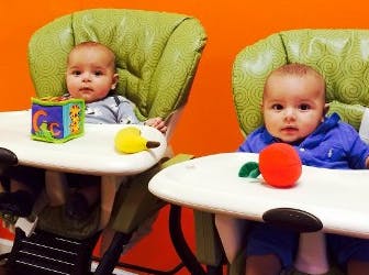 Two babies sitting in high chairs with toys