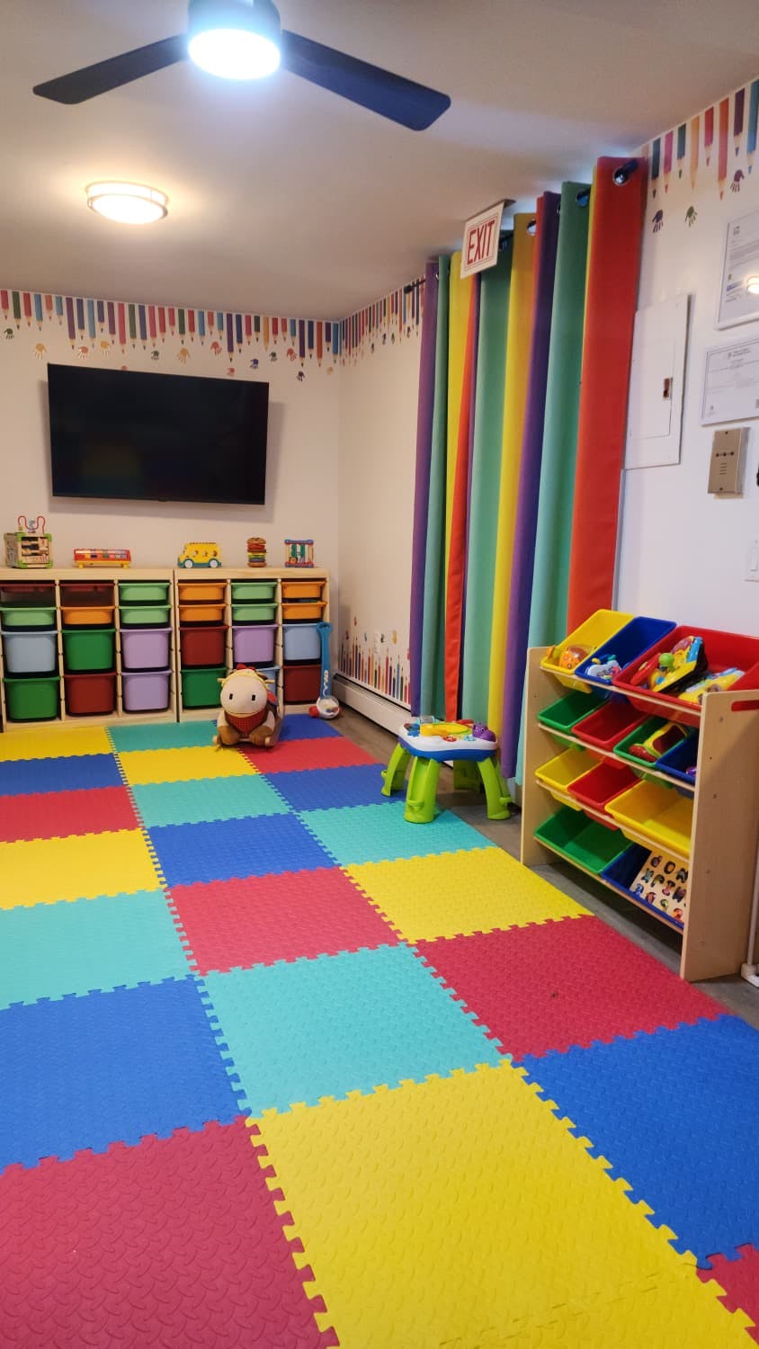 A playroom with colorful foam floor tiles, storage bins, and toys
