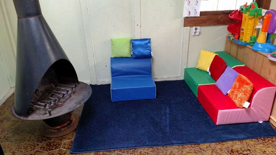 Playroom with a black fireplace, blue rug, and colorful soft play furniture