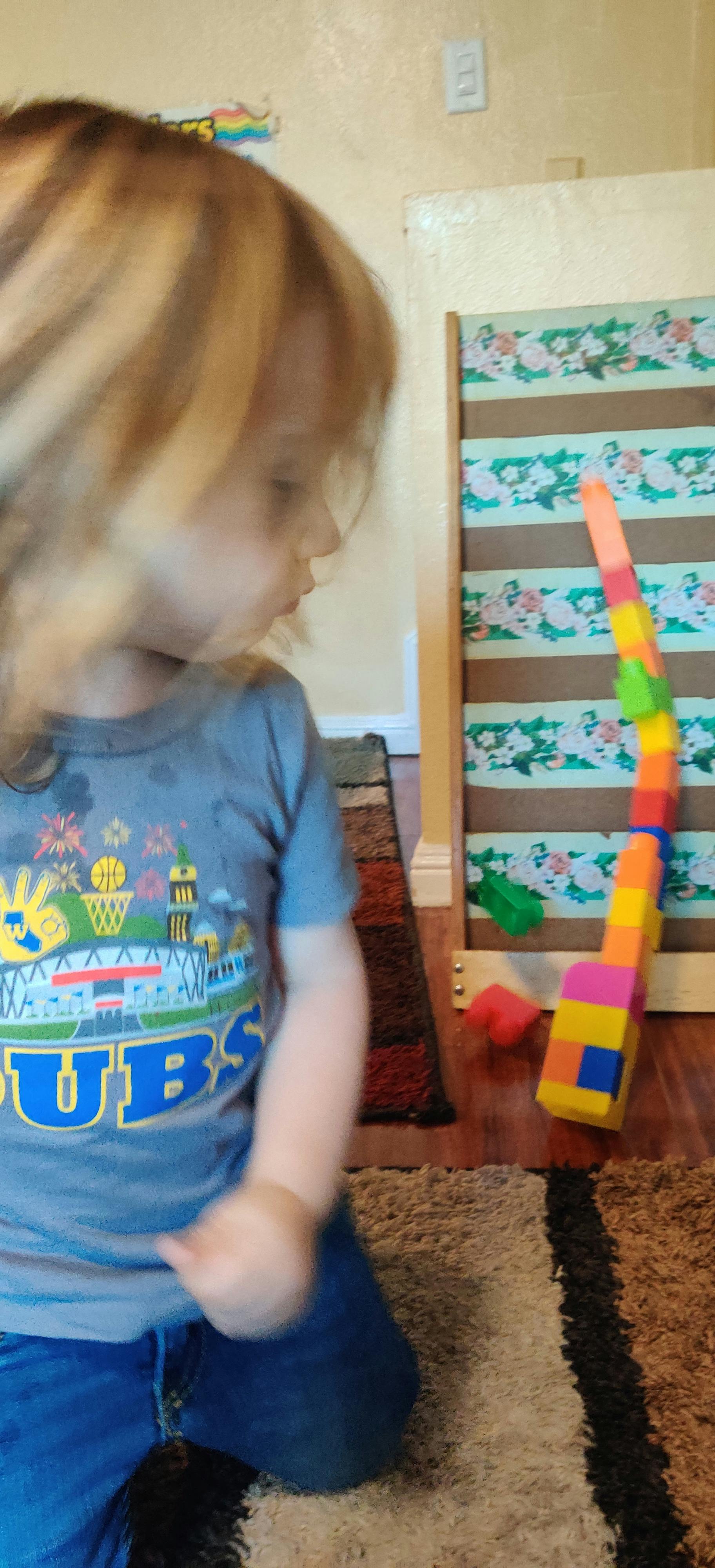Child kneeling on a rug looking at a tall stack of colorful blocks