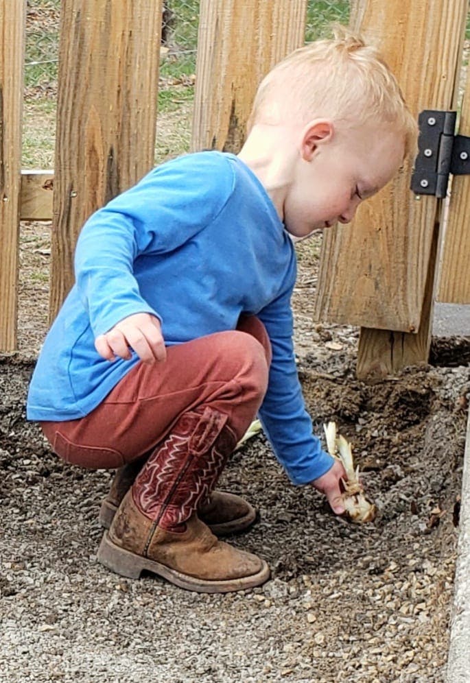 Child in boots crouching and planting in dirt