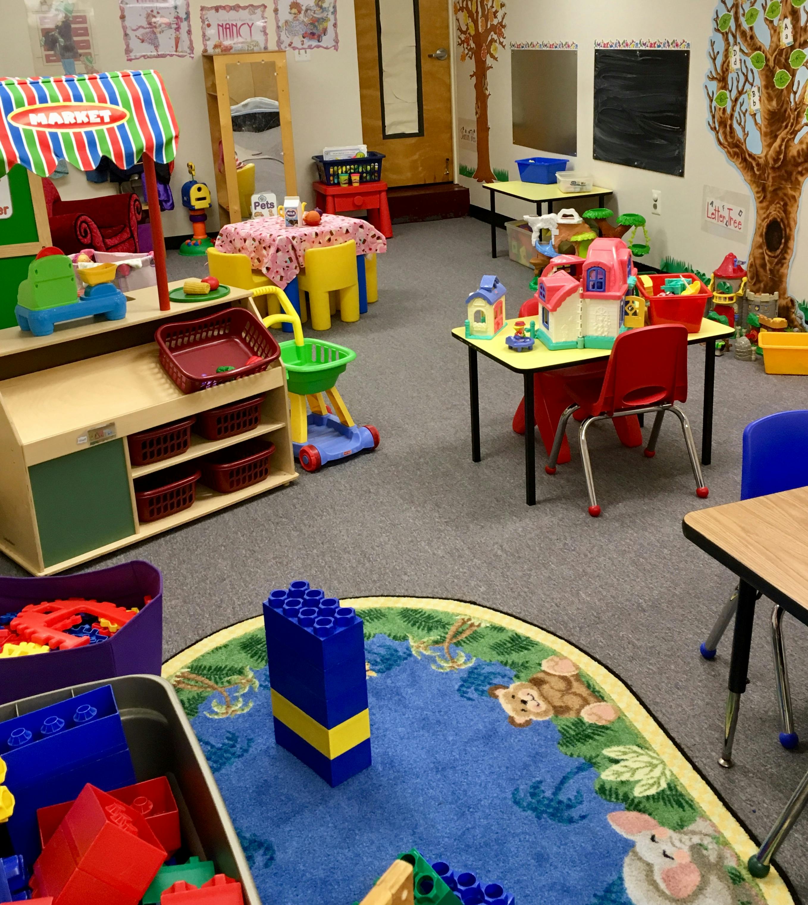 Playroom with small tables, chairs, and toys including a toy market stand