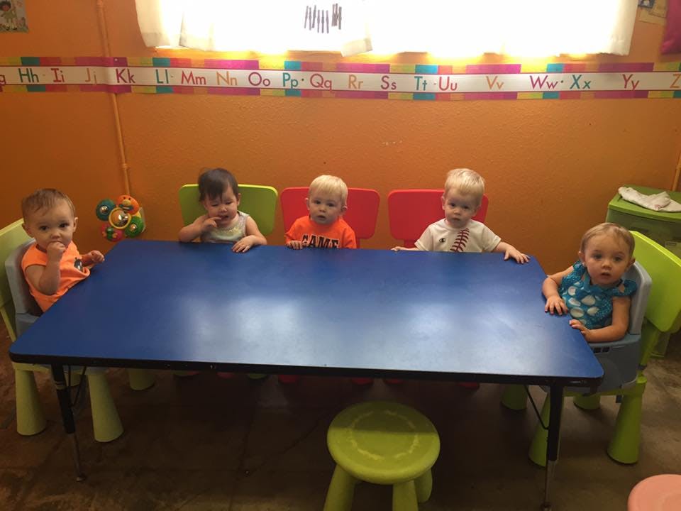 Five children sitting at a blue table in a classroom