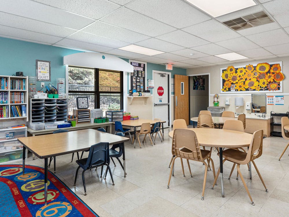 Classroom with tables, chairs, a bookshelf, and a window