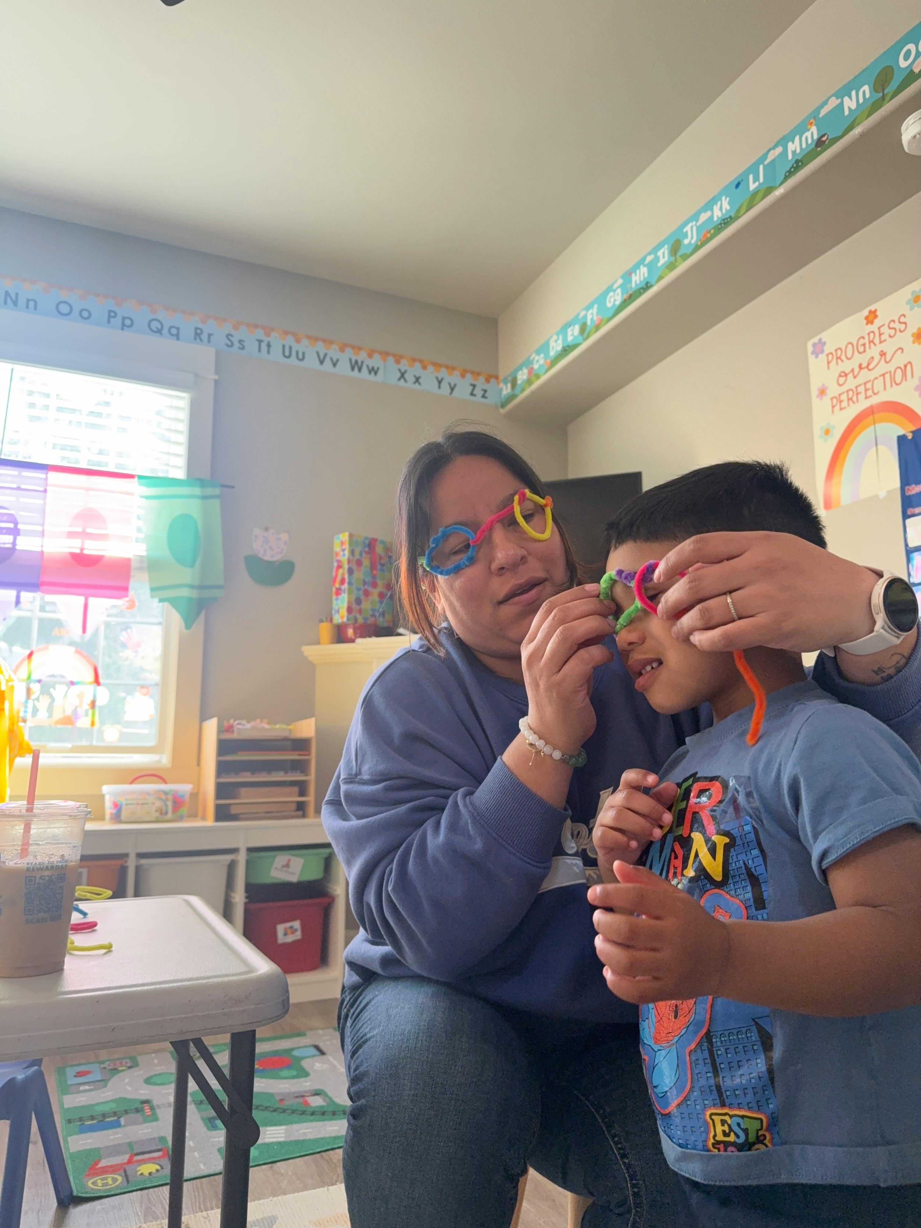 Adult and child wearing pipe cleaner glasses in a classroom