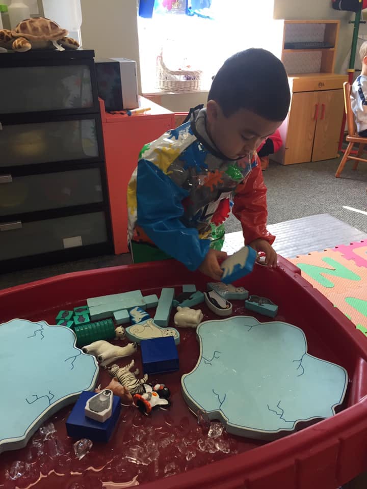 Child playing with toys in a red bin filled with water and ice