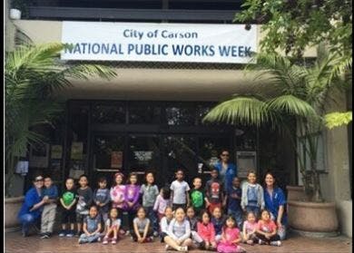 Adults and children posing in front of a building with a banner