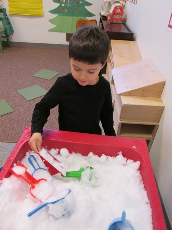 Child playing with scoops in a red bin filled with white material