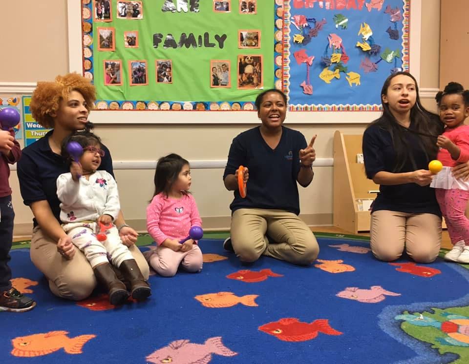 Adults and children kneeling on a rug with musical shakers
