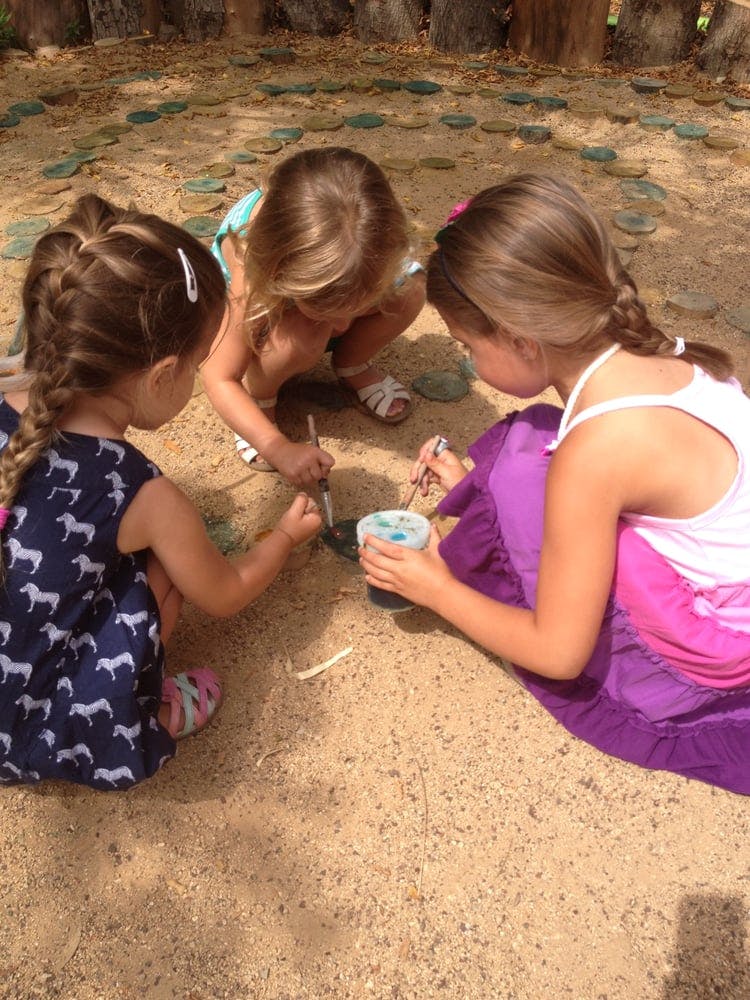Three children painting on the ground outdoors