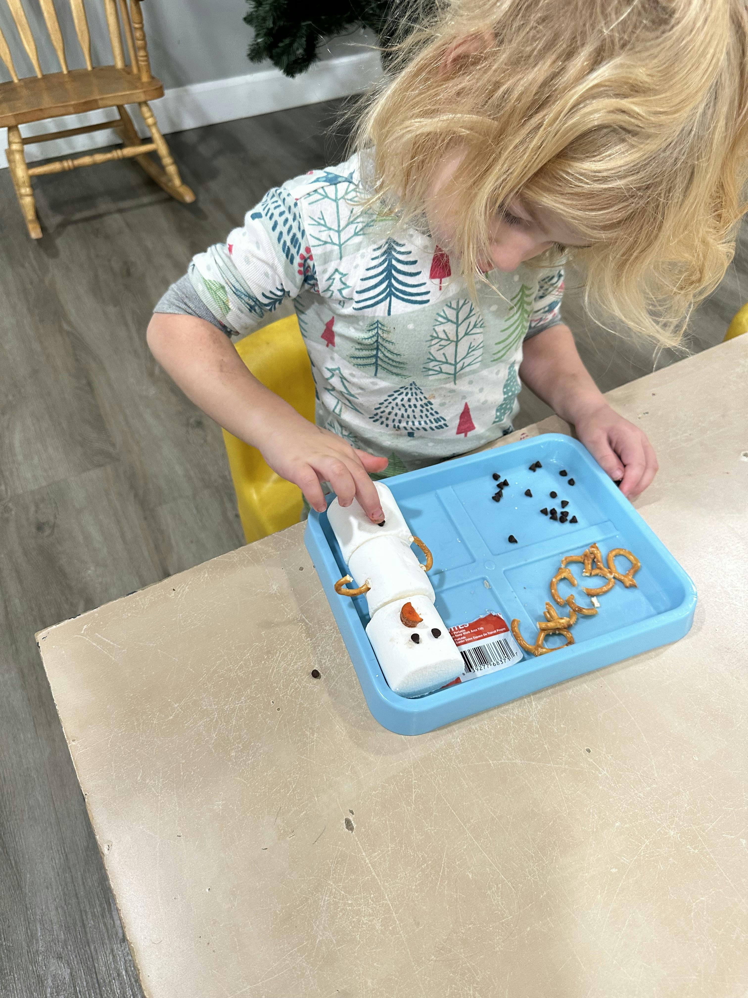 Child building a marshmallow snowman with pretzel and chocolate chip decorations