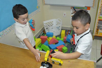 Two children playing with blocks and toy cars in a classroom