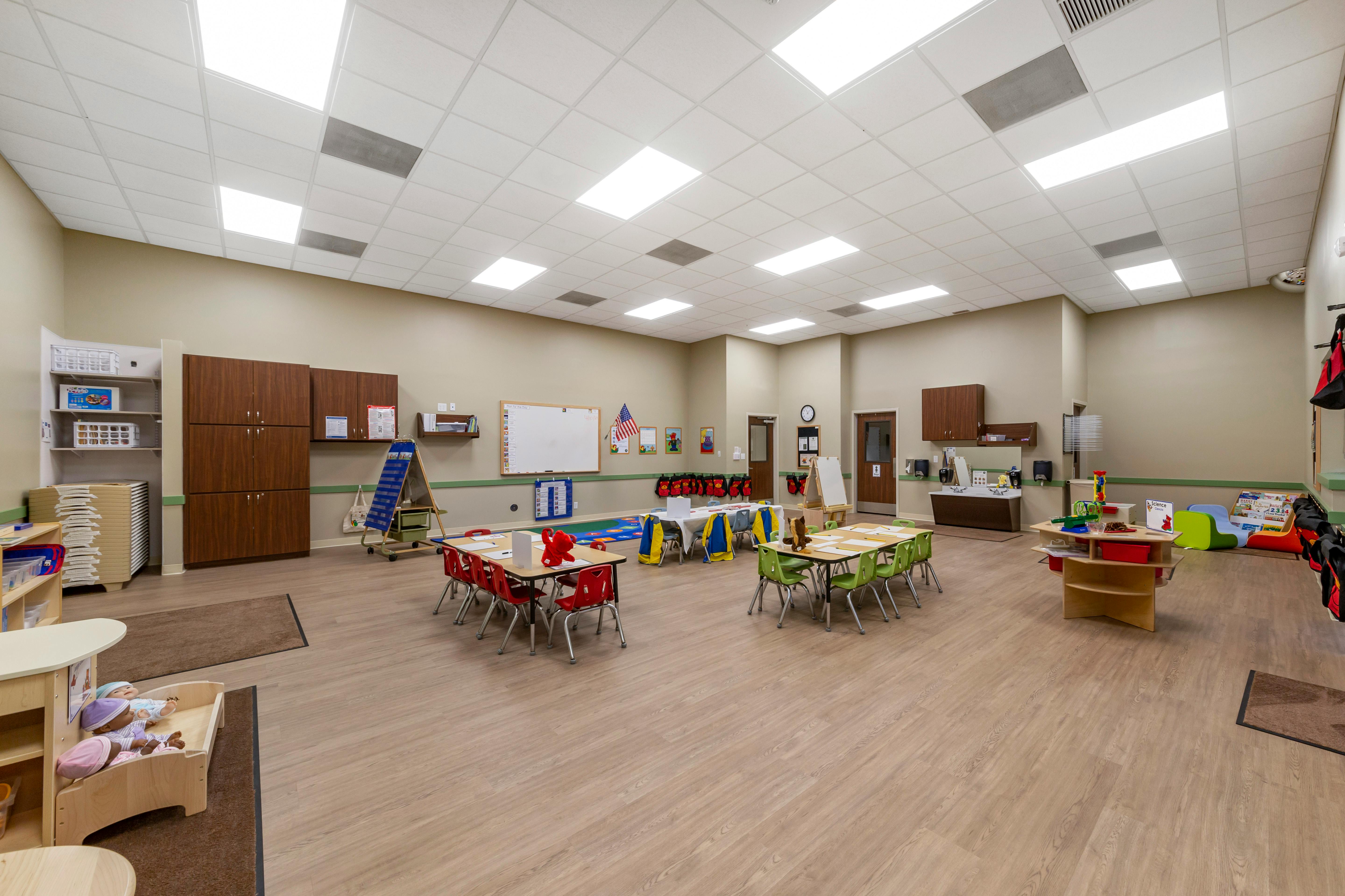 Classroom with small tables and chairs, whiteboards, and storage units