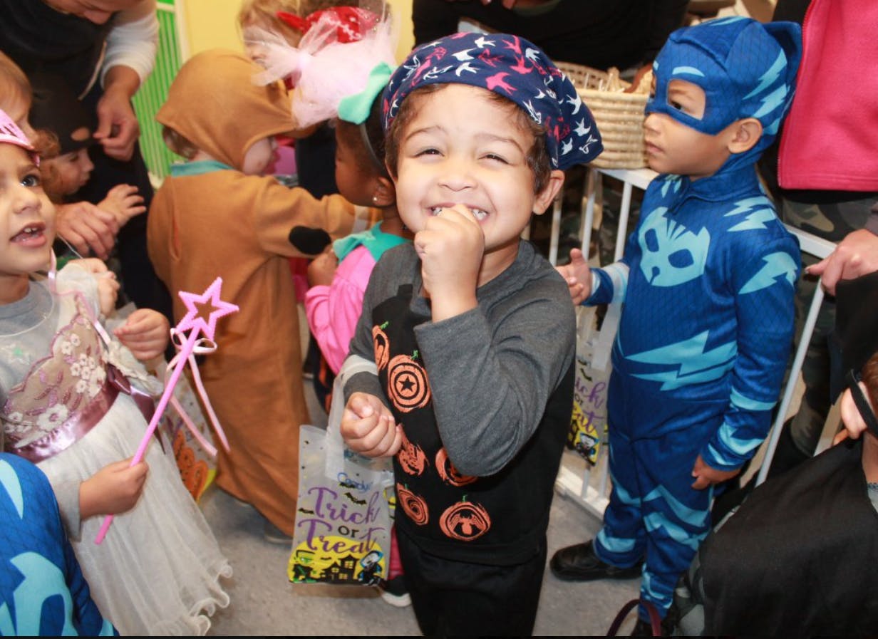 Child in costume smiling with hand near mouth, other children in costumes nearby