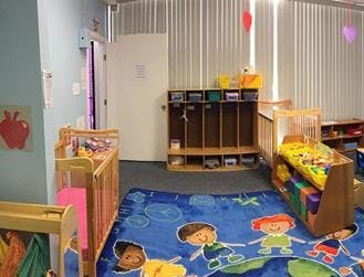 Nursery room with cribs, cubbies, and a colorful play mat
