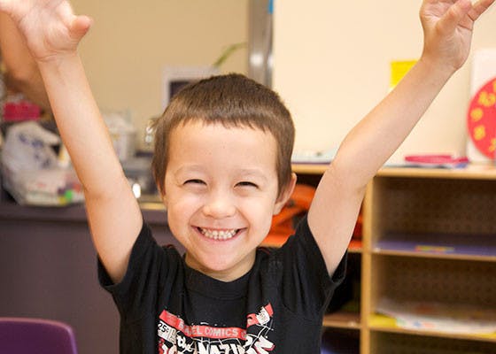 Child with arms raised in a classroom