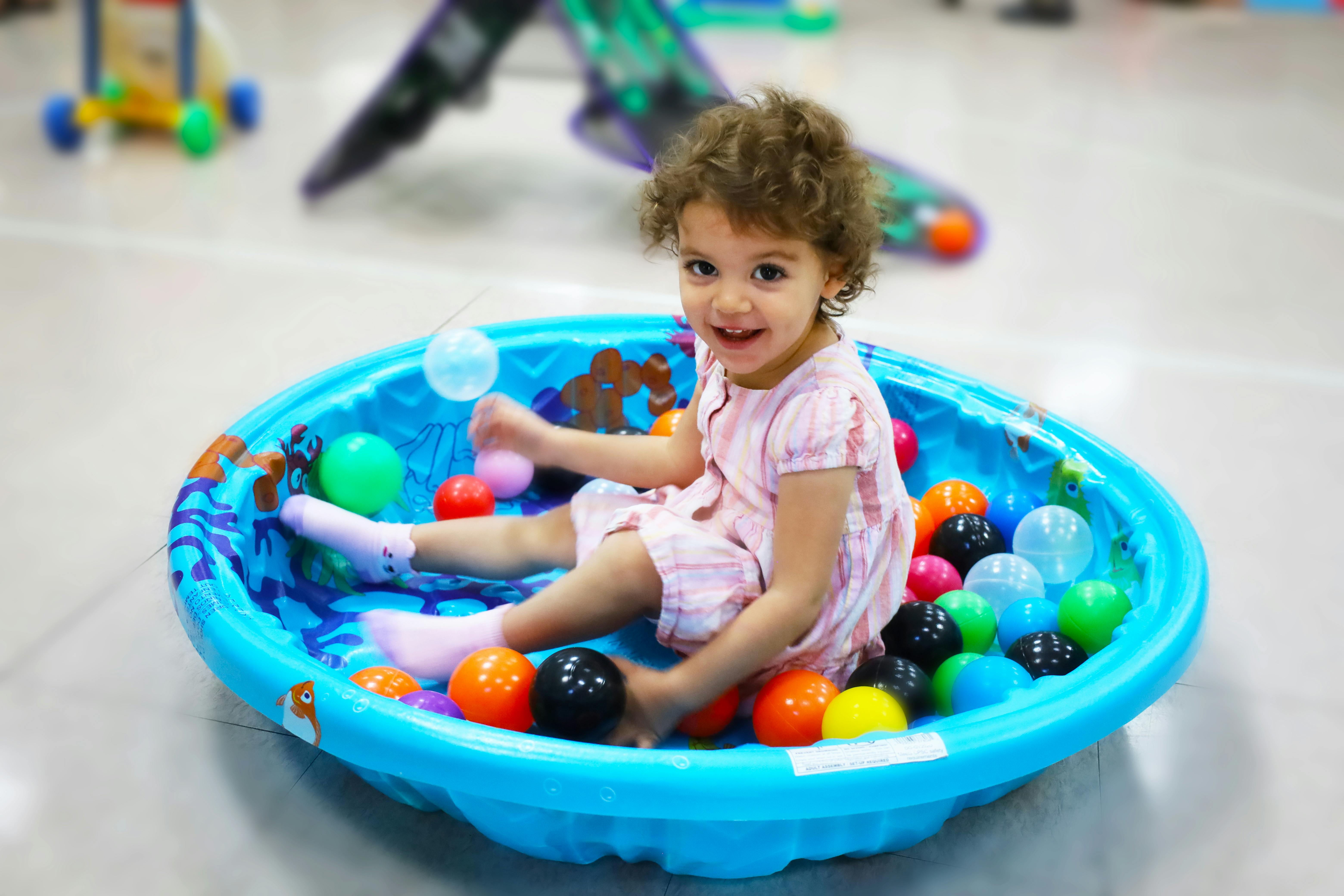 Child sitting in a blue ball pit with colorful balls