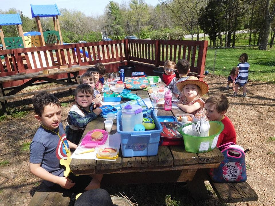 Children sitting at a picnic table with lunchboxes and drinks