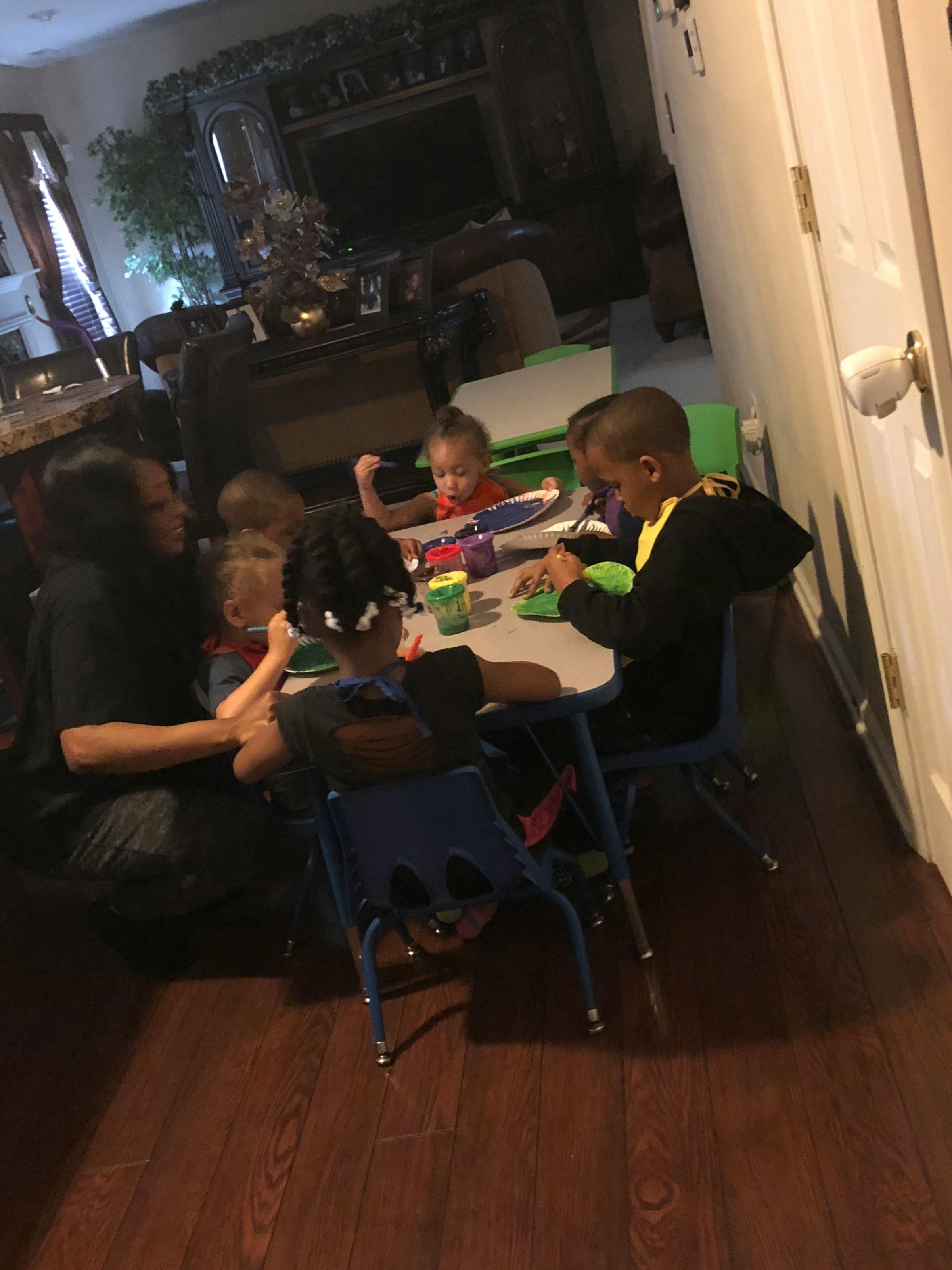 Adult and several children sitting at a table painting on paper plates