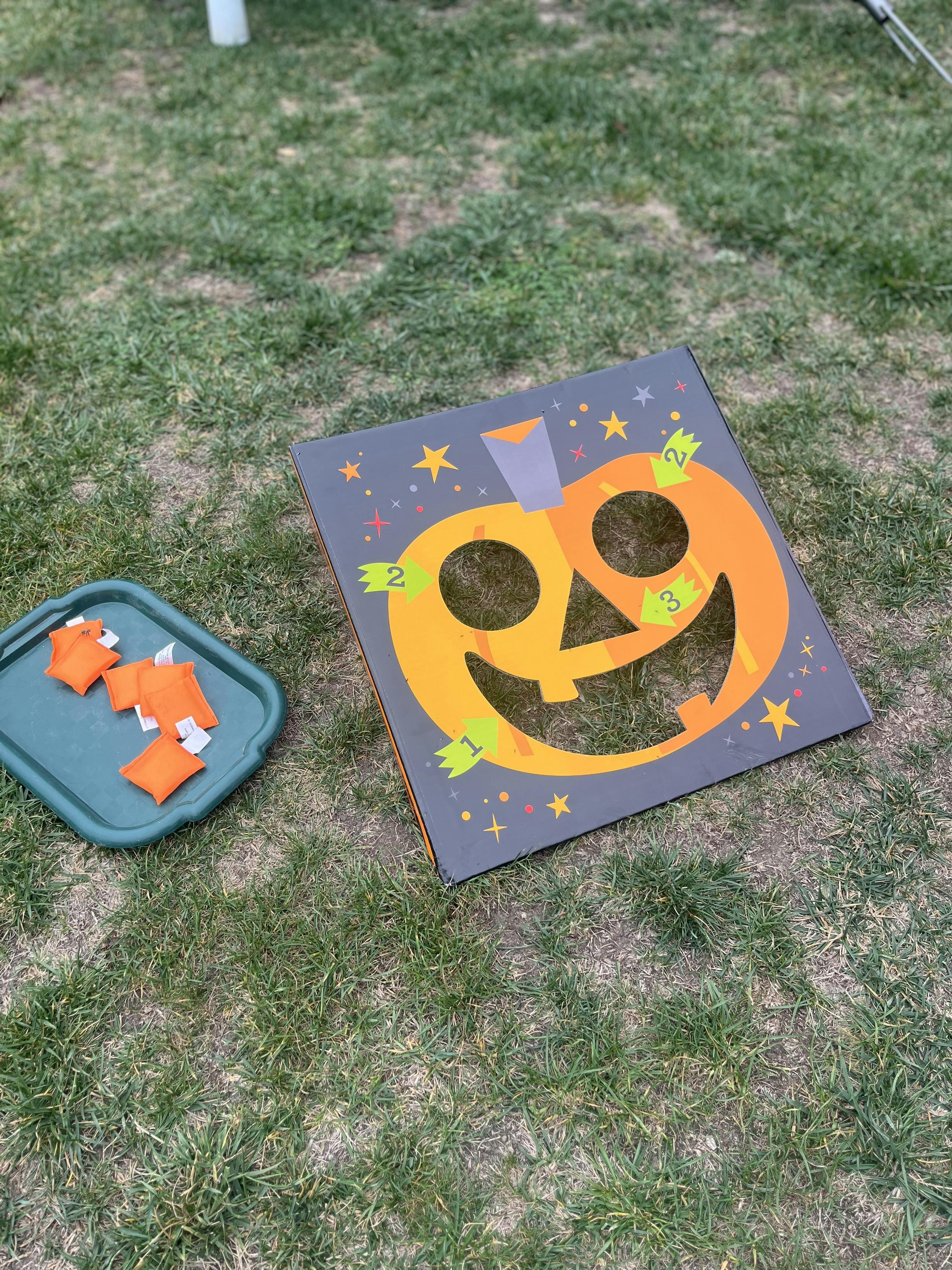 Pumpkin bean bag toss game on grass with bean bags on a tray