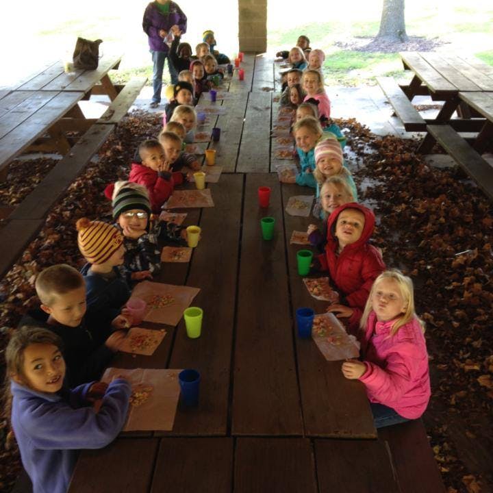 Children sitting at long picnic tables under a shelter