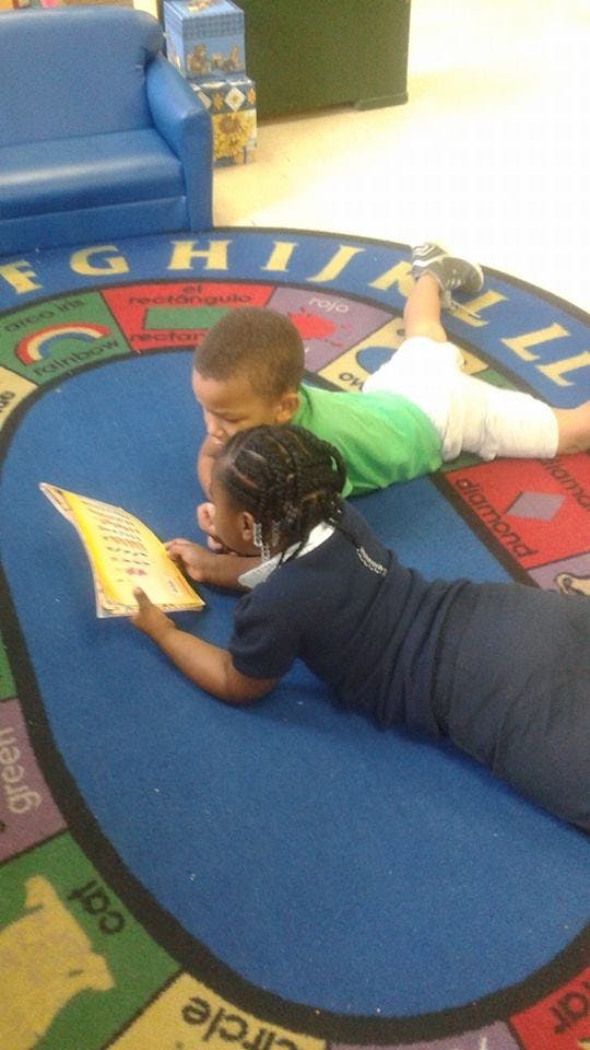 Two children lying on a rug, looking at a book