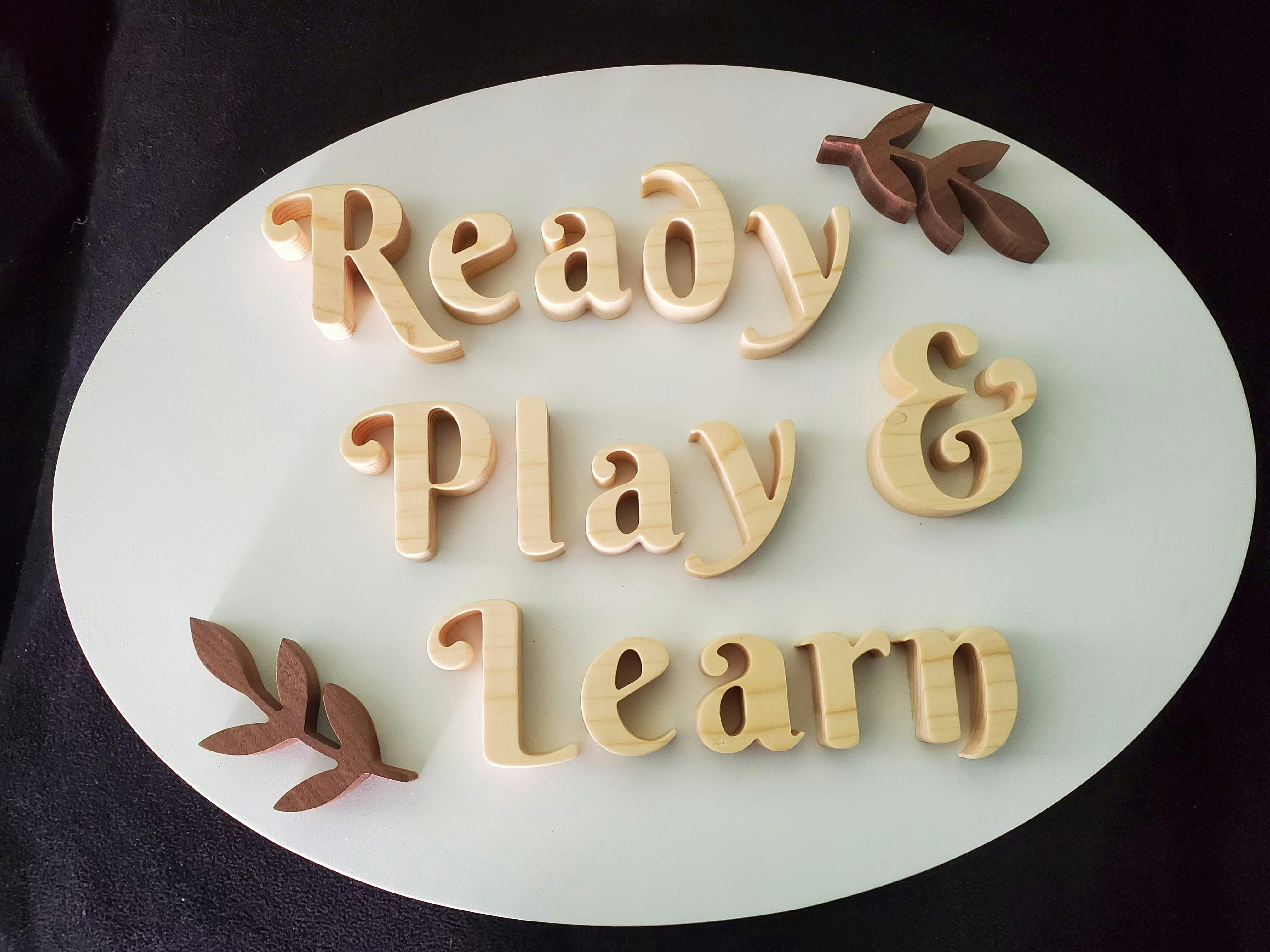Wooden cutouts spelling "Ready Play & Learn" with leaf accents on white board
