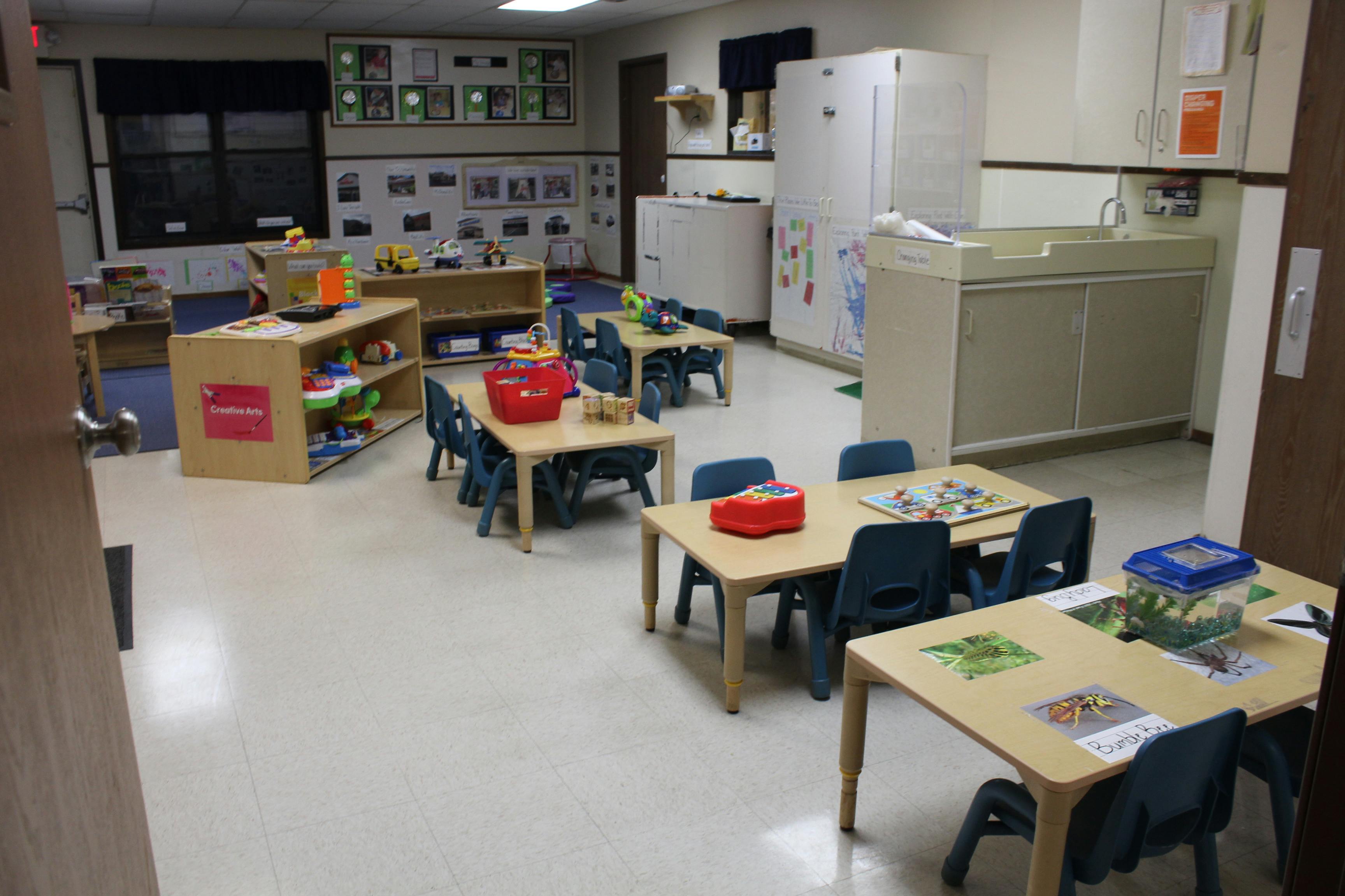 Classroom with small tables and chairs, shelves with toys, and a changing station