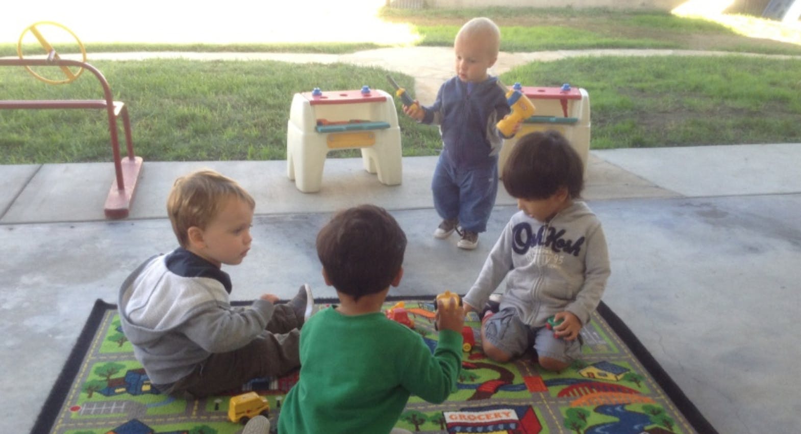 Four children playing on a rug outdoors
