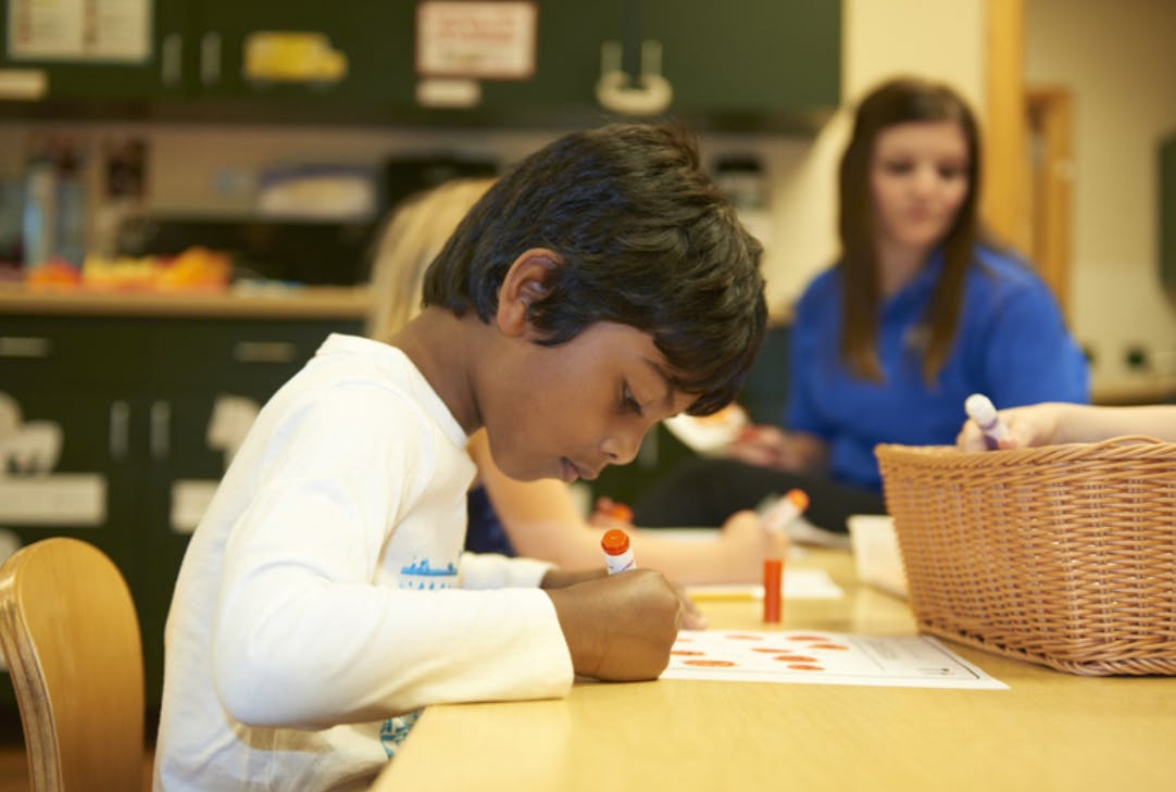 Child writing at a table in a classroom